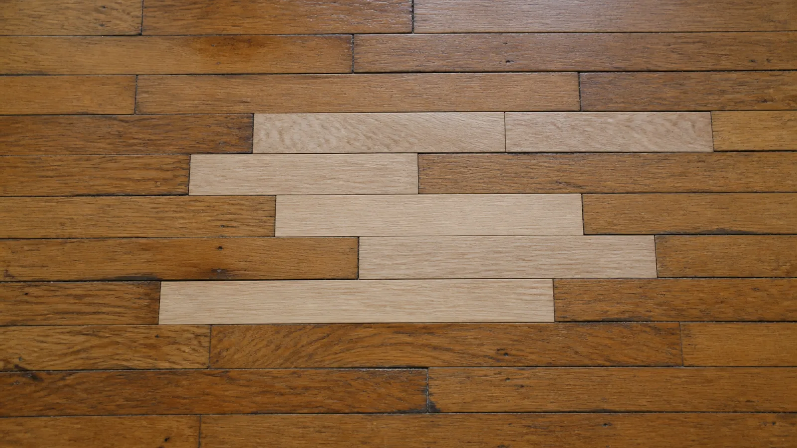 Several new pale unfinished oak boards woven into an older amber oak strip floor in a staggered pattern